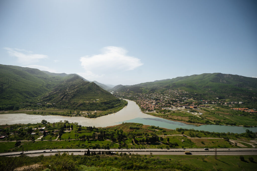 Panoramic view of green mountains lying around old city and river confluence with road nearby on sunny summer day